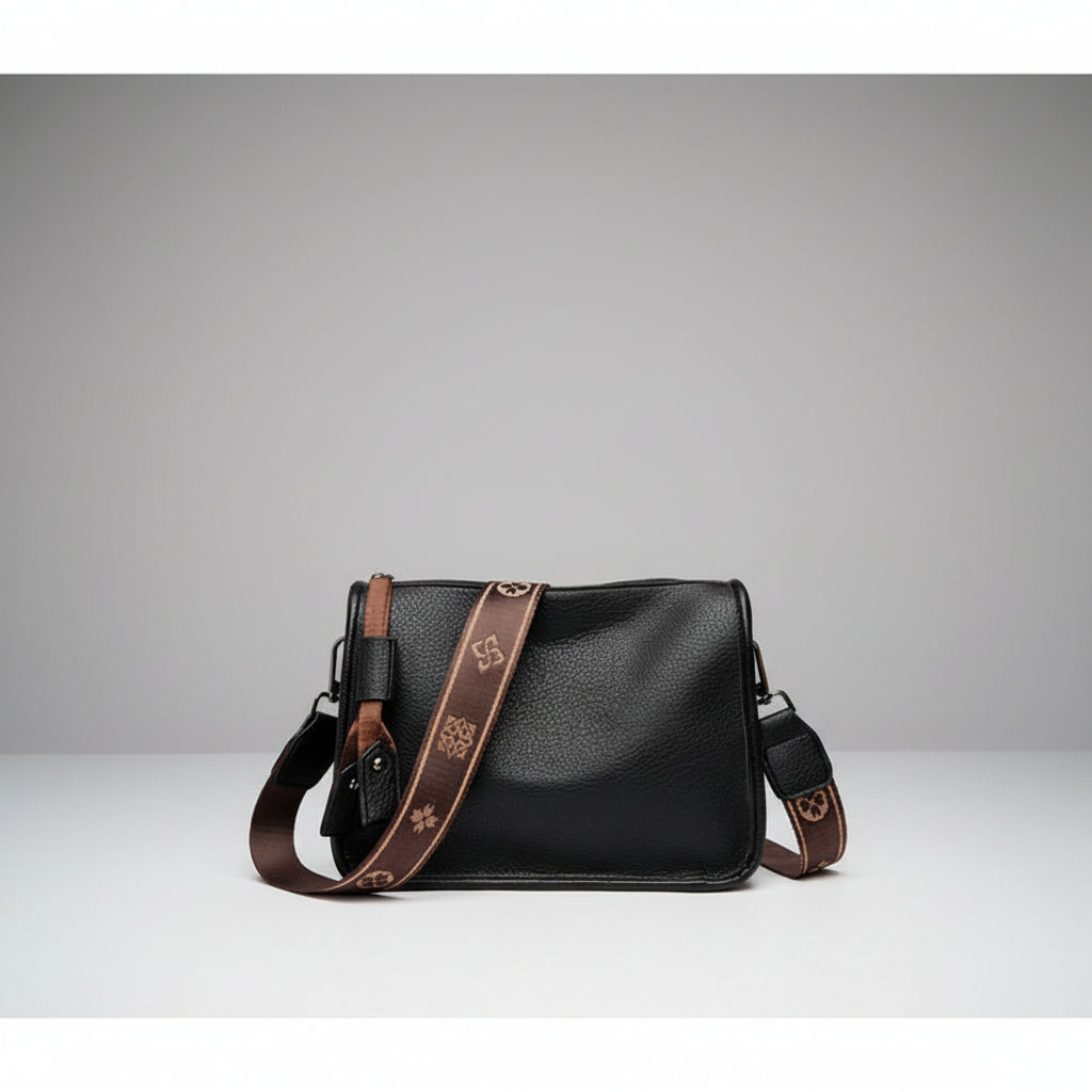 Auralis Genuine Cowhide Crossbody Bag in black, front studio view showcasing rectangular silhouette, zip-top closure, and patterned adjustable strap