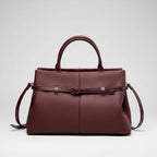 Front view of a wine red genuine leather tote bag with a sleek and sophisticated design, highlighted by the central buckle accent