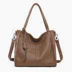 Front view of a brown vegan leather tote bag featuring a minimalist design with a central tassel detail and elegant handles