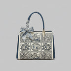 Front view of the Elisandra embroidered tote bag showcasing an intricate floral embroidery design with a stylish blue bow on the handle