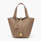 Lunelia Vegan Leather Bucket Bag in brown, front studio view showcasing tapered bucket silhouette, gold padlock charm, and base feet
