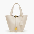 Lunelia Vegan Leather Bucket Bag in white, front studio view showcasing tapered bucket silhouette, twin handles, and gold padlock charm with base feet