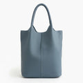 Front view of blue cowhide leather tote bag with minimalist design, featuring a central seam and sturdy handles